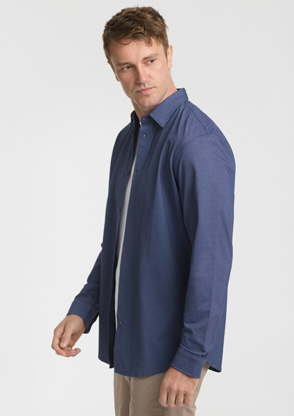 Side view of a man wearing a navy blue button-down shirt over a white T-shirt, standing against a light background.