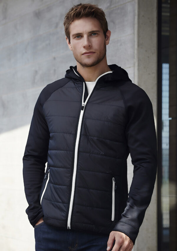 fbj515m_worn_00 Man wearing a black quilted puffer jacket with white zippers, standing against a concrete wall.