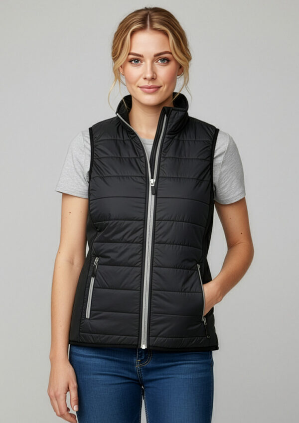 Woman wearing a black quilted sleeveless puffer vest over a gray T-shirt and blue jeans, standing against a neutral background.