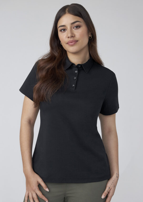 Portrait of a woman wearing a black polo shirt with a buttoned collar, standing against a light gray background.
