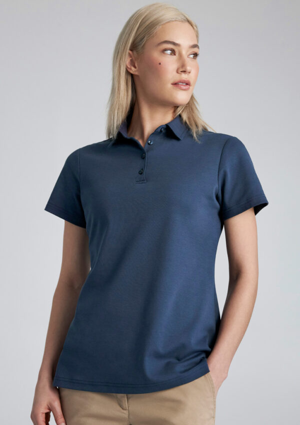 Woman wearing a navy polo shirt with short sleeves and beige pants, looking to the right.