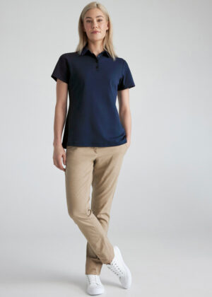 Woman standing in a navy polo shirt, khaki pants, and white sneakers in a neutral studio backdrop.
