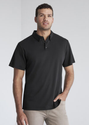 Man wearing a black short-sleeve polo shirt and beige pants, standing against a light neutral backdrop.