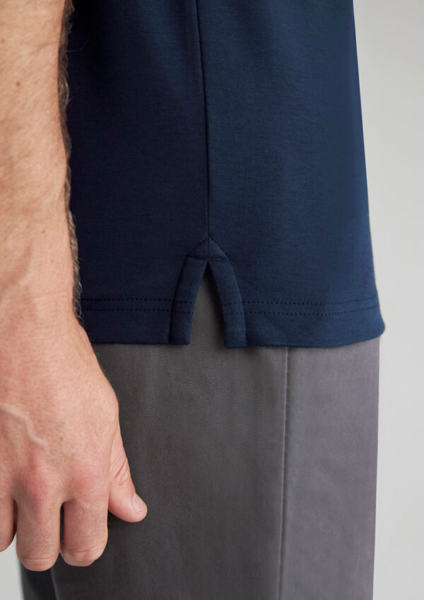 Close-up of a navy polo shirt hem with a small side vent over gray pants