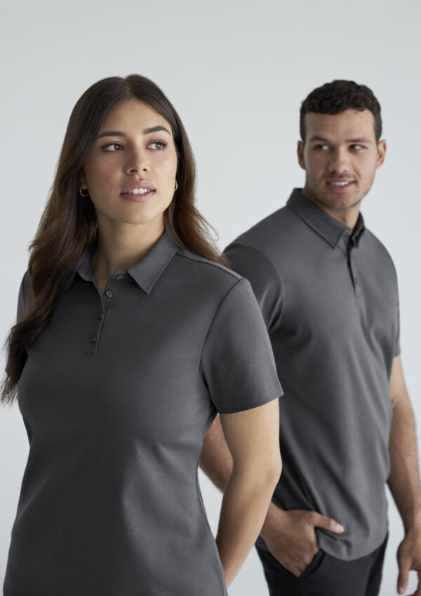 Two models wear matching dark gray polo shirts, standing side by side against a light background, looking off to the left.