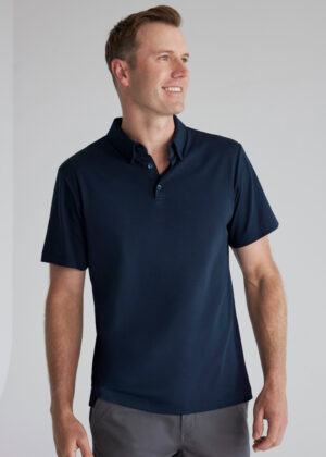 Man wearing a navy polo shirt, standing against a light gray background and looking to his left.