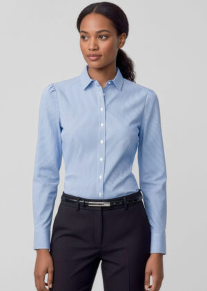 Woman wearing a light blue striped button-down shirt and black dress pants, standing against a light gray background.