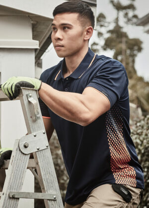 Man wearing gloves and a navy polo shirt stands on a ladder, performing outdoor maintenance near a building.