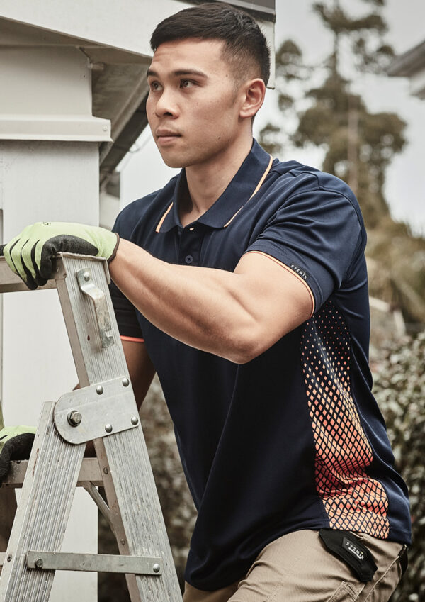 Man wearing gloves and a navy polo shirt stands on a ladder, performing outdoor maintenance near a building.