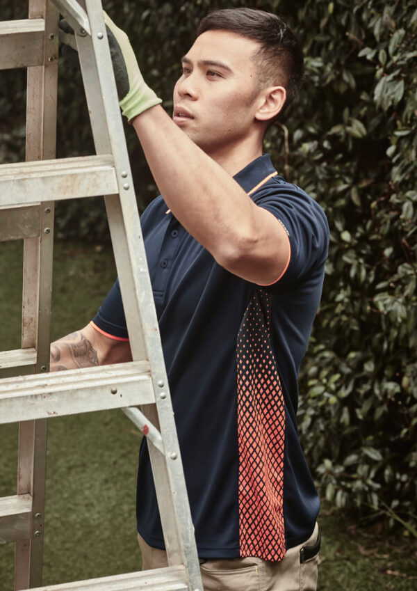 Man in a navy polo with orange trim stabilizes a metal ladder outdoors in a garden.