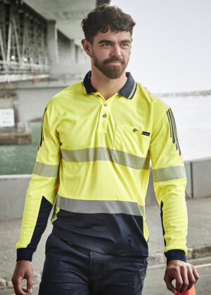 Bearded man in a bright yellow high-visibility polo with reflective stripes stands near a waterfront in an industrial area.