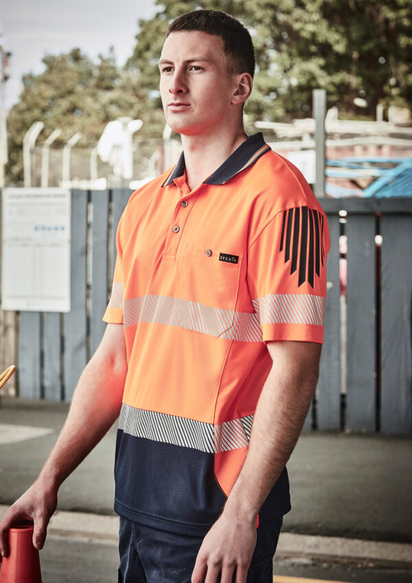 fbzh555_worn_01.jpg Man in a bright orange high-visibility polo with reflective stripes, standing outdoors near a fence.