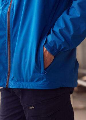 Close-up of a person wearing a bright blue windbreaker with their hand in the pocket near the zipper edge.