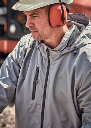 Worker wearing a white hard hat, orange ear protection, and a gray protective jacket outdoors at a site.