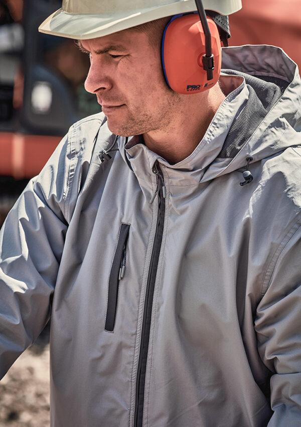 Worker wearing a white hard hat, orange ear protection, and a gray protective jacket outdoors at a site.