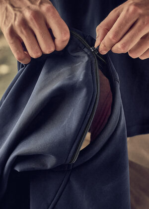 Close-up of hands zipping a navy blue jacket, pocket opening showing brown lining inside.
