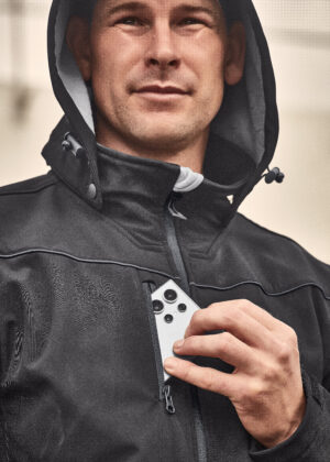 Man in a black hooded jacket places a white smartphone with multiple cameras into a chest pocket.
