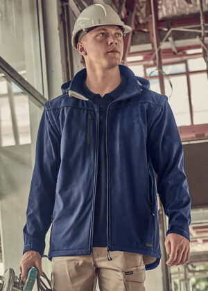 Young construction worker wearing a white hard hat and blue jacket on a building site.