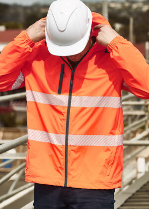 Construction worker in an orange high-visibility jacket with reflective stripes, adjusting a white hard hat at a construction site.