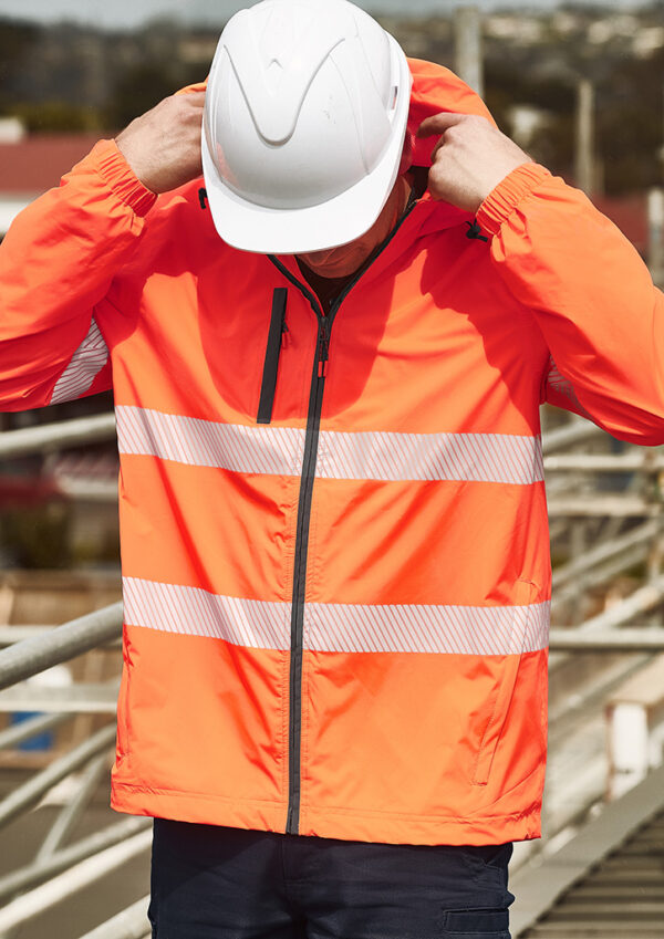 Construction worker in an orange high-visibility jacket with reflective stripes, adjusting a white hard hat at a construction site.