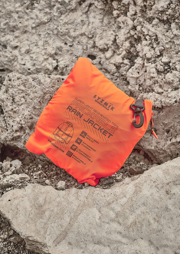 Bright orange packable rain jacket in its waterproof stuff sack on rough rocky terrain.