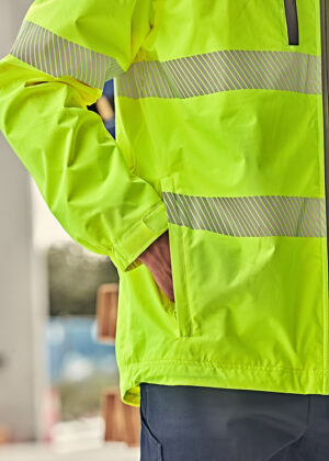 Close-up of a neon-yellow high-visibility jacket with reflective stripes and a hand tucked into a side pocket.
