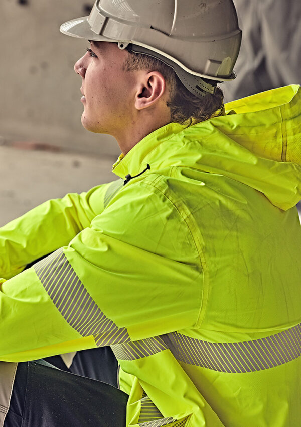 Side profile of a construction worker wearing a neon-yellow safety jacket and hard hat, sitting and looking to the left on a worksite.
