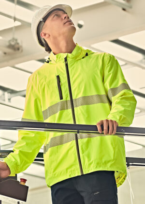 Construction worker in a neon high-visibility jacket and white hard hat looking up while holding a railing in an industrial setting.