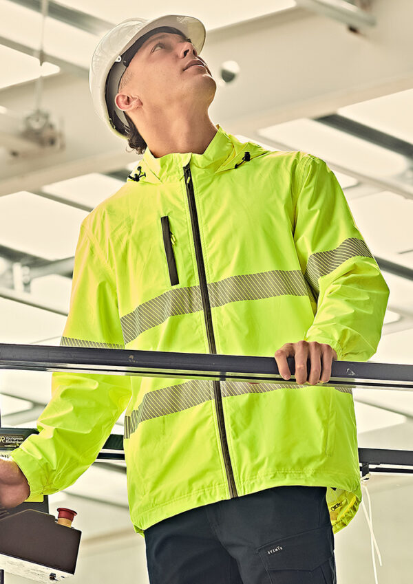 Construction worker in a neon high-visibility jacket and white hard hat looking up while holding a railing in an industrial setting.