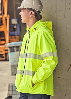 Construction worker in neon safety jacket and hard hat leaning against a wall at a construction site.