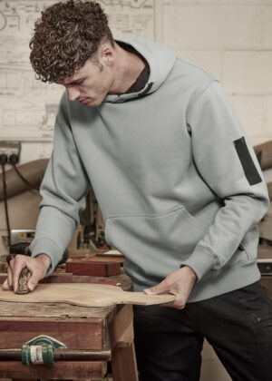 Young man in a gray hoodie planing a wooden board on a workbench in a woodshop.