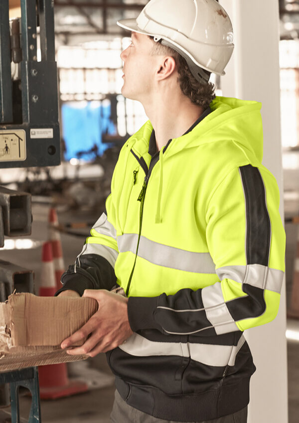 Construction worker in a high-visibility jacket and hard hat placing a cardboard box on a pallet in a warehouse or industrial setting.