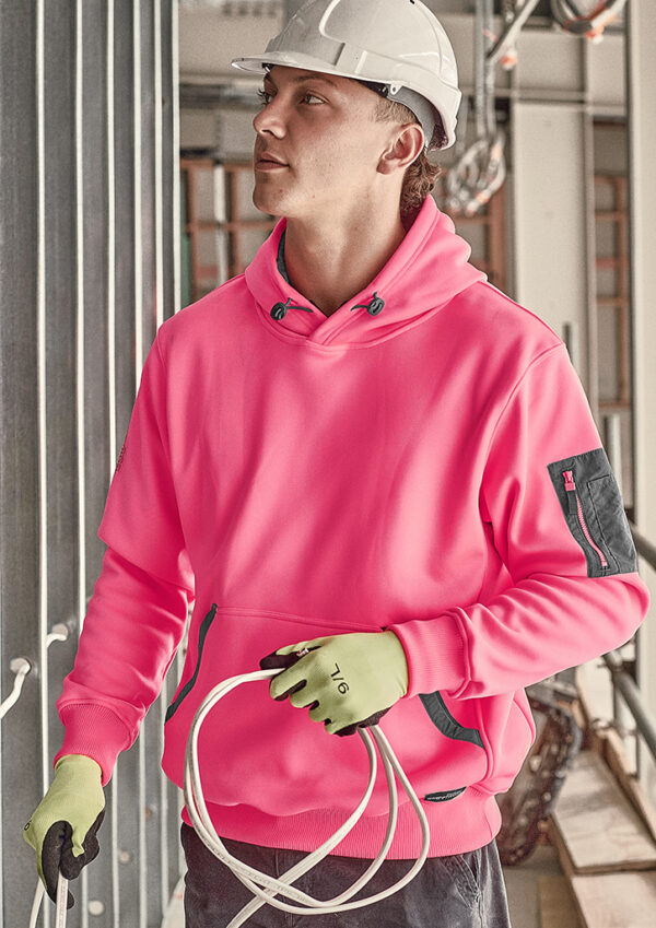 Construction worker in a pink hoodie and white hard hat holding a coil of white cable on a construction site, gloves on hands.